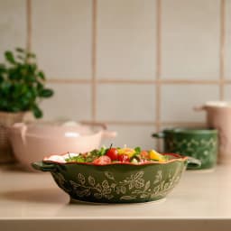 Green porcelain baking dish with handles, cream interior, and red floral patterns on a white background - view 1