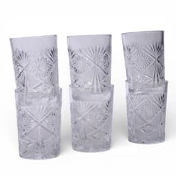 Four clear patterned glass drinking cups, two stacked, on a light tiled surface with plants and pink bowls in background. - view 2