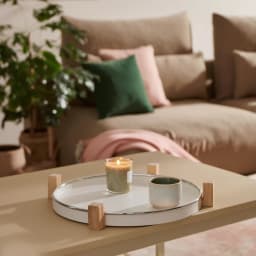 Round white porcelain serving tray with light wood stand on a kitchen counter, holding a small jar and a woven item. - view 4