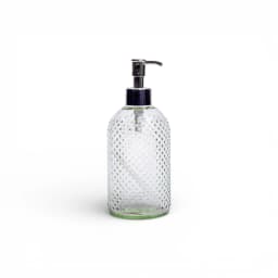 Clear glass soap dispenser with a silver pump and a textured dotted pattern, filled with light yellow liquid soap, on a bath… - view 2