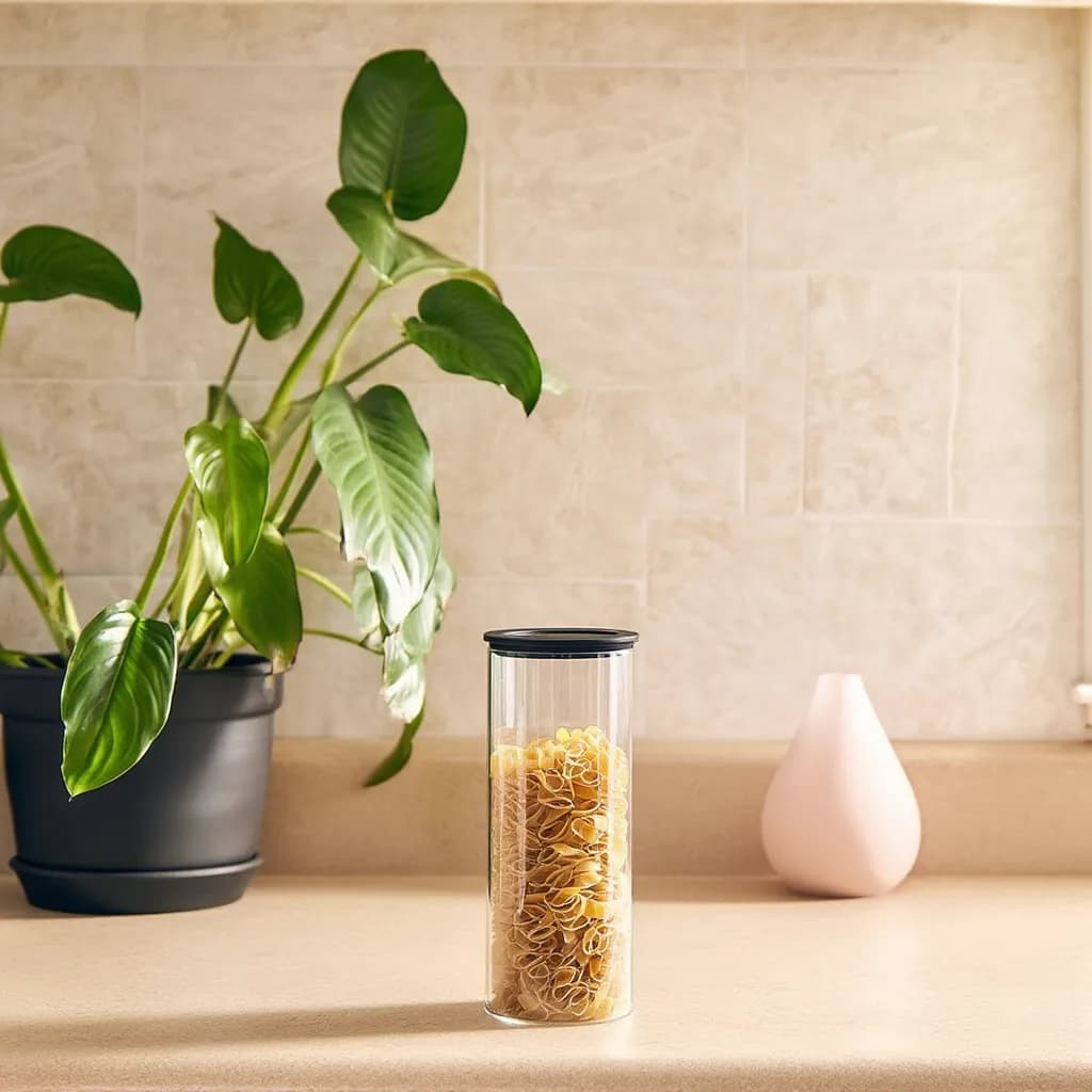 Single clear cylindrical glass storage jar with a black lid on a white background