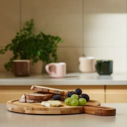 Light brown round bamboo wood cutting board with an integrated rectangular handle on a white background. - view 1
