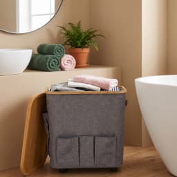Grey fabric storage hamper with a light brown bamboo wood lid and three front pockets, on wheels. - view 1