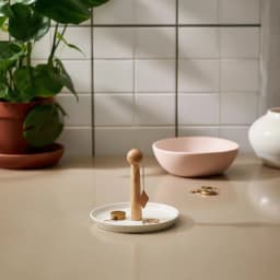 Round white porcelain serving plate with a tall, light wood central handle, on a beige table in a living room setting. - view 8
