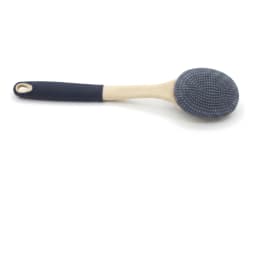 Long-handled silicone bath brush with grey bristles and a beige and dark grey handle, resting on a green soap dish with foam. - view 2