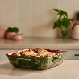 Rectangular porcelain baking dish with wavy red rim, cream interior with red floral pattern, and dark green exterior with wh… - view 4