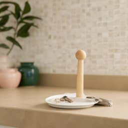 Round white porcelain serving plate with a tall, light wood central handle, on a beige table in a living room setting. - view 4