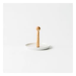 Round white porcelain serving plate with a tall, light wood central handle, on a beige table in a living room setting. - view 2