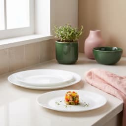 A collection of white round glass dinner plates of various sizes, with one plate in the foreground holding a small salad por… - view 3