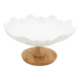 White porcelain serving bowl with a wavy, petal-like rim, sitting on a round light brown wood base, on a white background. - view 3