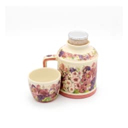 Cream porcelain jug with a handle and a matching cup stacked on top, both adorned with pink and purple floral patterns, on a… - view 4