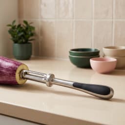 Silver metal vegetable peeler with a black handle peeling an orange carrot on a beige kitchen counter - view 3