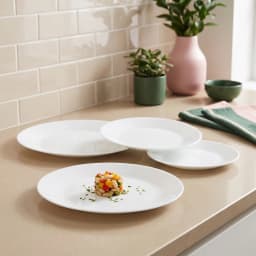 A collection of white round glass dinner plates of various sizes, with one plate in the foreground holding a small salad por… - view 1
