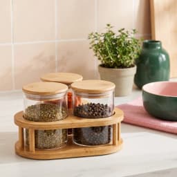 Three clear glass storage jars with light brown wooden lids, arranged on a light brown wooden stand, on a white background. - view 1