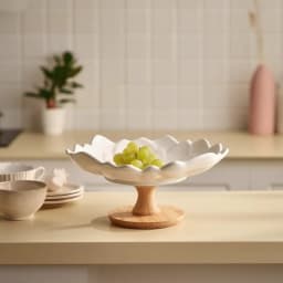 White porcelain serving bowl with a wavy, petal-like rim, sitting on a round light brown wood base, on a white background. - view 1