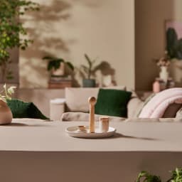 Round white porcelain serving plate with a tall, light wood central handle, on a beige table in a living room setting. - view 5