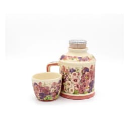 Cream porcelain jug with a handle and a matching cup stacked on top, both adorned with pink and purple floral patterns, on a… - view 5