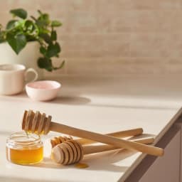 Five light brown wooden honey dippers with spiral grooves, standing upright against a white background. - view 1
