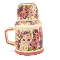 Cream porcelain jug with a handle and a matching cup stacked on top, both adorned with pink and purple floral patterns, on a… - view 3