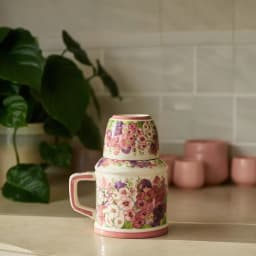 Cream porcelain jug with a handle and a matching cup stacked on top, both adorned with pink and purple floral patterns, on a… - view 6