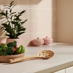 Light brown wooden slotted spoon with multiple drainage holes and a hanging hole on the handle, on a white background. - view 1