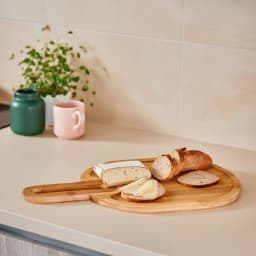 Light brown oval wood serving board with a handle and two recessed compartments on a white background. - view 1