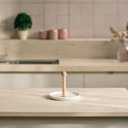 Round white porcelain serving plate with a tall, light wood central handle, on a beige table in a living room setting. - view 9