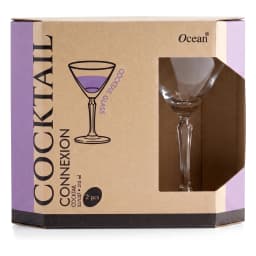 Two clear glass cocktail glasses with green liquid on a wooden table next to a plant and product box, with sofa in backgroun… - view 4