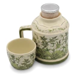 Cream porcelain jug with green floral pattern and matching cup inverted on top, on a kitchen counter. - view 4