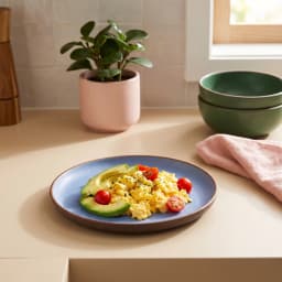 Round blue melamine plate with a brown rim, holding scrambled eggs, avocado, and cherry tomatoes. - view 1